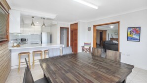 A modern kitchen with white cabinets, a wooden dining table, and bar stools.