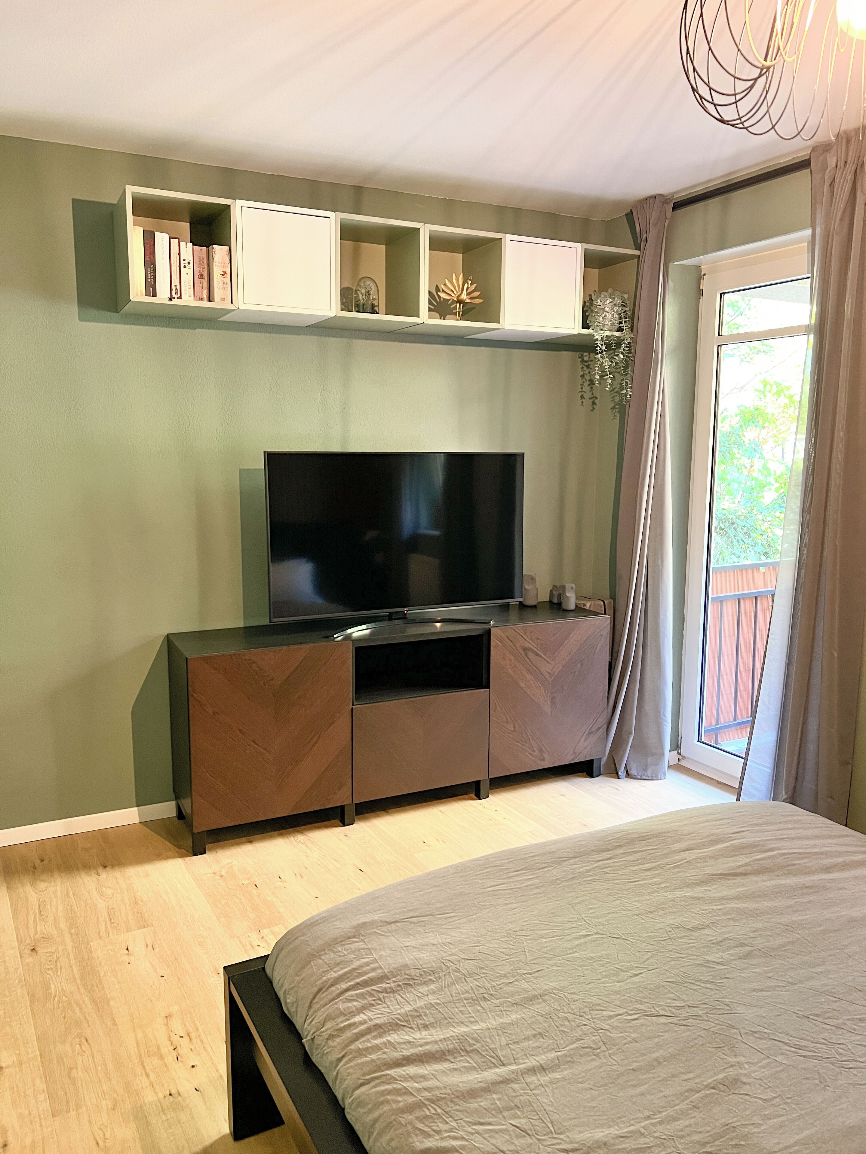 A bedroom with a bed, a TV on a cabinet, and a window with curtains.