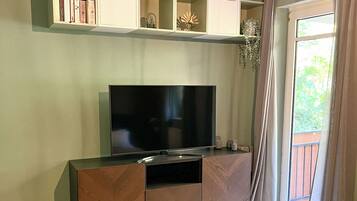 A bedroom with a bed, a TV on a cabinet, and a window with curtains.