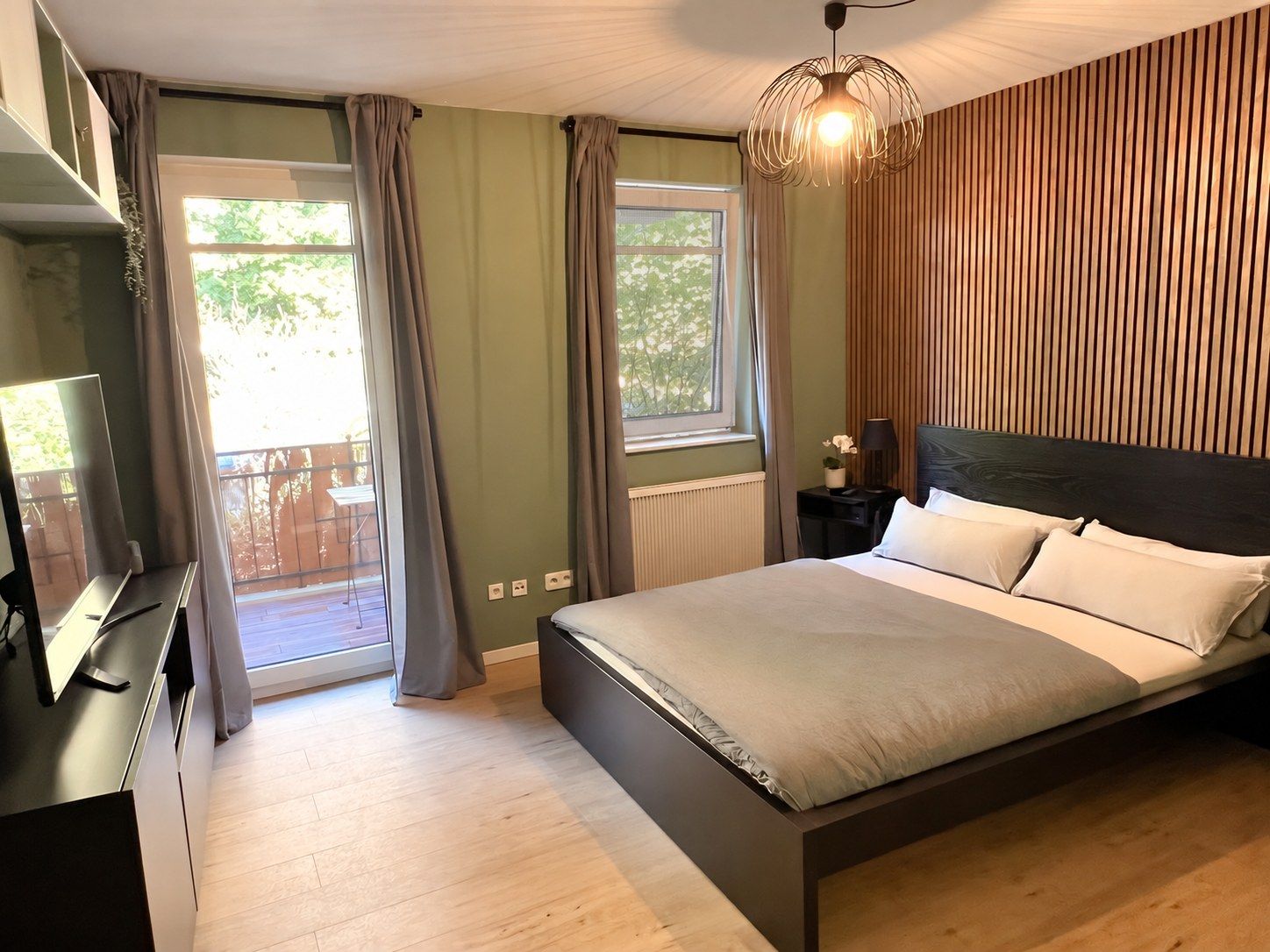 Ein Schlafzimmer mit einem Bett, einem Schreibtisch, einem Stuhl, einem Fenster mit Vorhängen und einer Pendelleuchte.