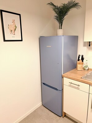 A kitchen with a blue Liebherr refrigerator, a wooden countertop, a sink, and a framed picture of a llama. - JUPAS° Red Rock Home – 2 Balconies & Carport (Trier)