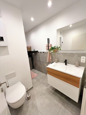 A modern bathroom with a white sink, a mirror, and a toilet. - JUPAS° Red Rock Home – 2 Balconies & Carport (Trier)