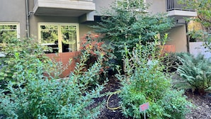 A residential building with a balcony, a garden with various plants, and a sign indicating a specific area. - JUPAS° | Red Rock Home - Balcony & Parking lot (Trier)
