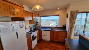 A compact kitchen with wooden cabinets, a stove, a sink, and a view of the ocean.