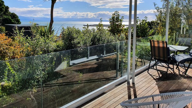 A balcony with a glass railing, a wooden deck, and a view of the sea.