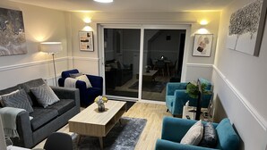 Una sala de estar moderna con un sofá gris, sillones color turquesa, una mesa de centro de madera y un comedor con platos y cubiertos blancos.