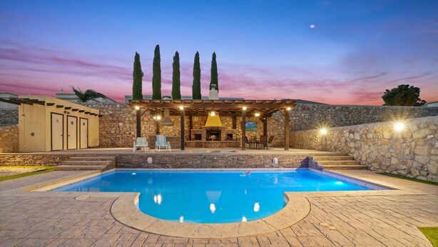 Una piscina con cubierta de piedra, un muro de piedra y una pérgola con luces.