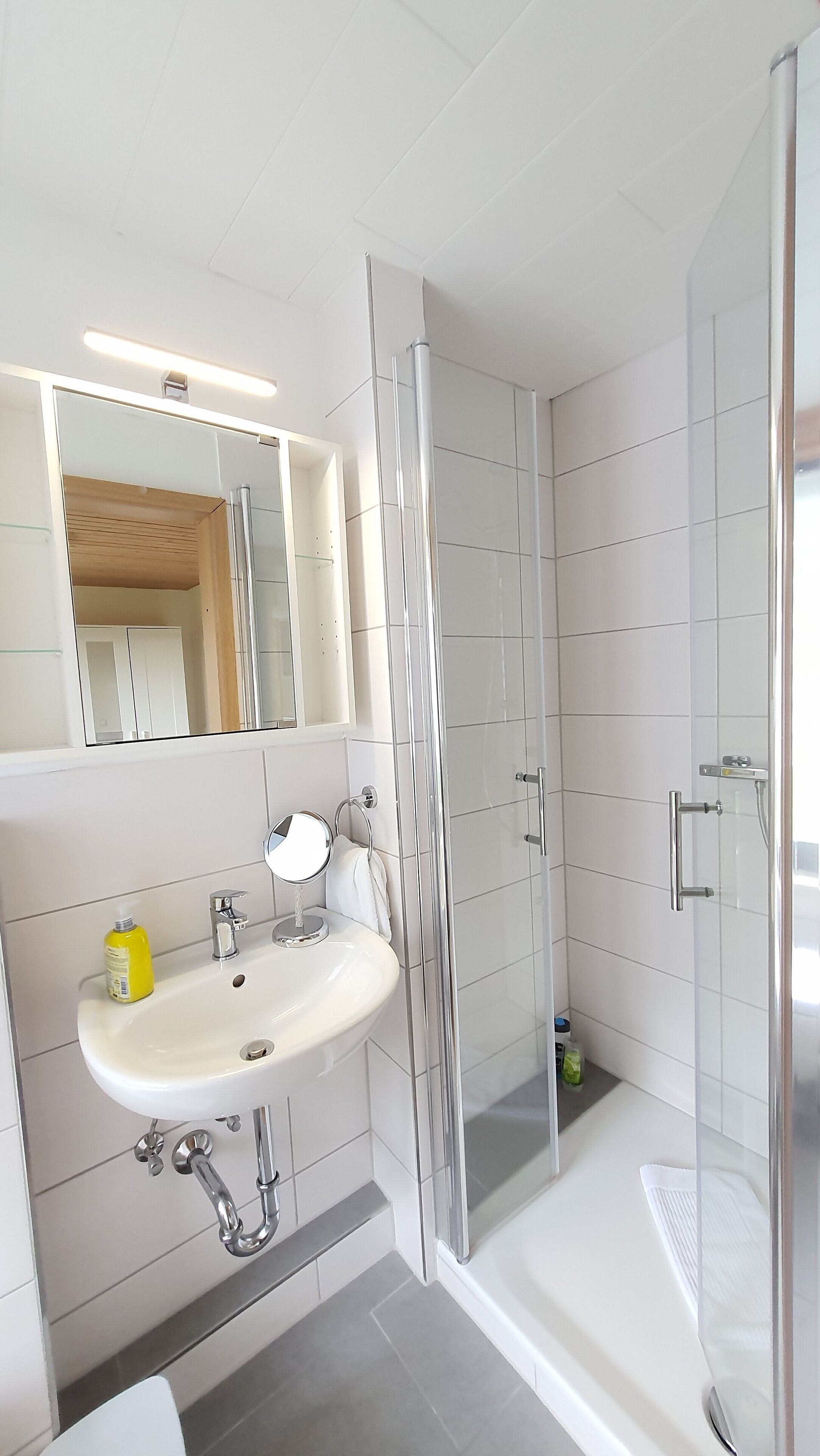 Un baño moderno con lavamanos blanco, espejo y cabina de ducha de vidrio.