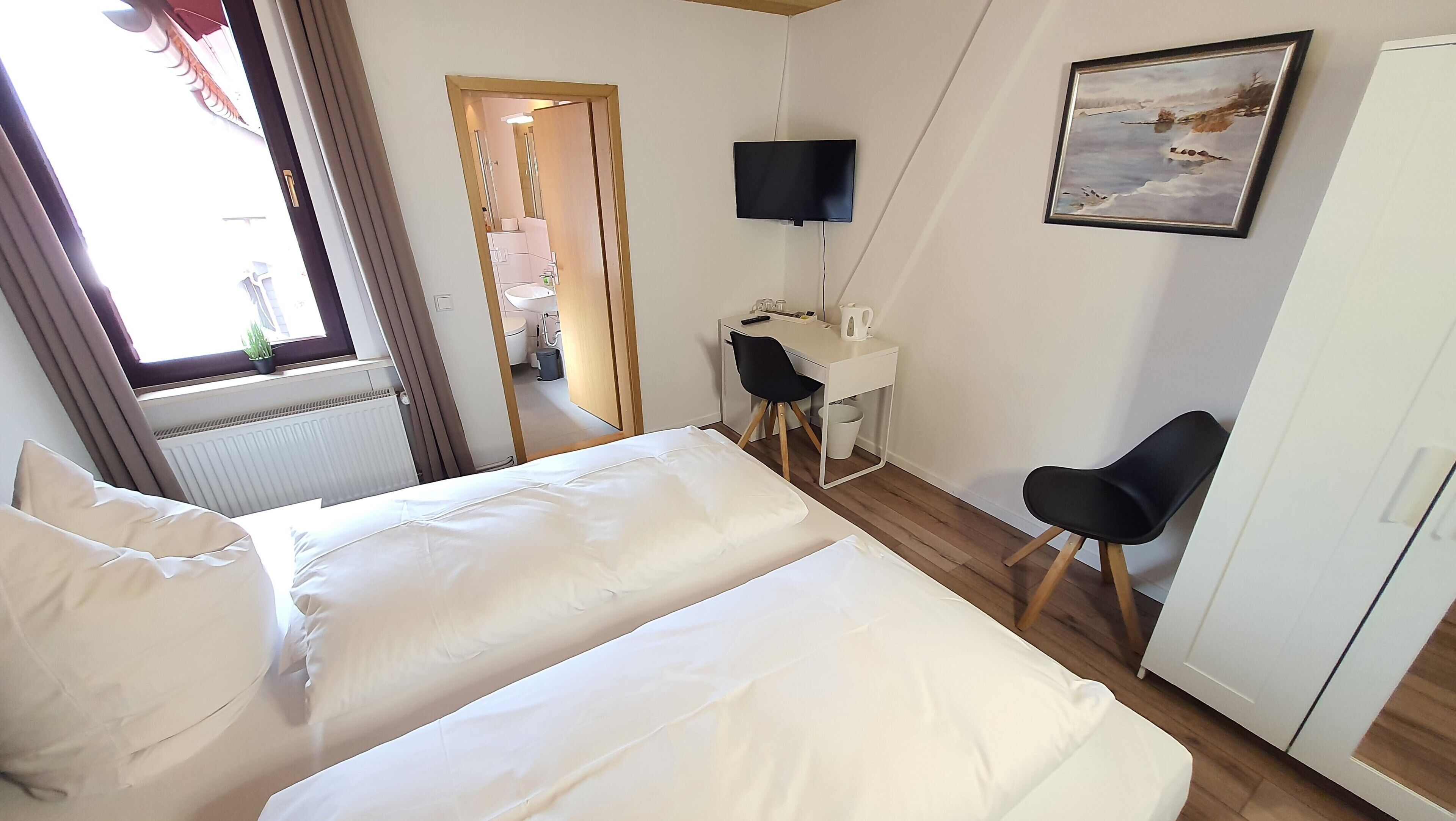 Habitación de hotel con cama, escritorio, silla, televisor y un cuadro en la pared.