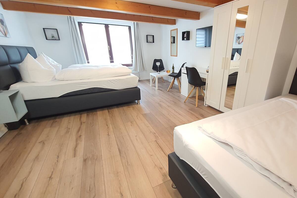 Une chambre d’hôtel avec deux lits, un bureau, une chaise et une grande fenêtre.