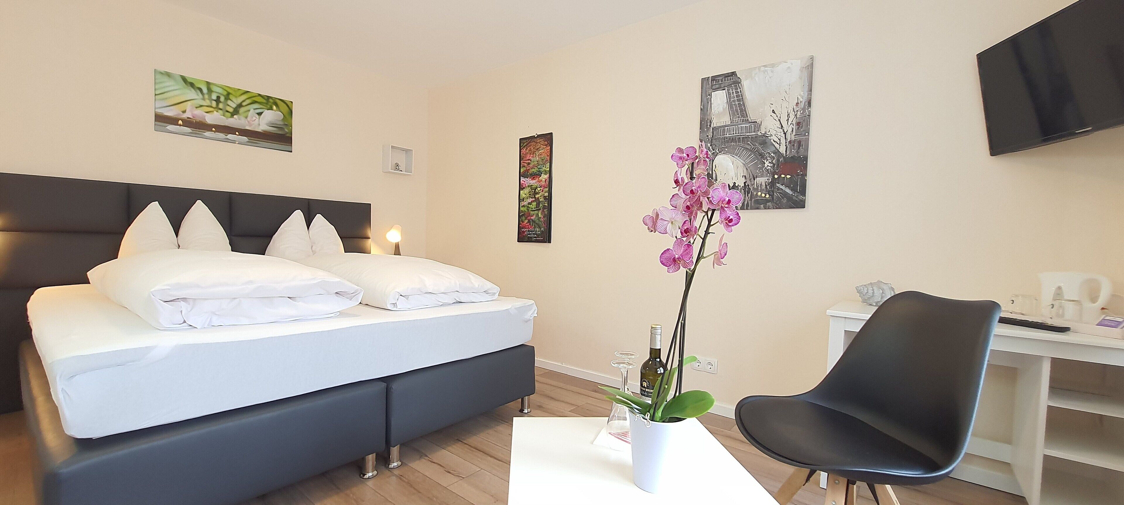 Una camera d'albergo con un letto, una scrivania, una sedia, una pianta e opere d'arte alle pareti.