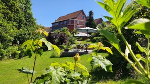 A garden with a patio, a red building, and a clear sky. - Hotel Schneiderhof (Braunlage)