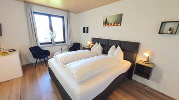 Habitación de hotel con una cama grande, un escritorio con silla, una ventana con cortinas y un cuadro colgado en la pared.