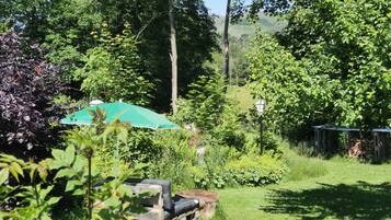 A garden with a green umbrella, a wooden bench, and a wooden structure in the background.