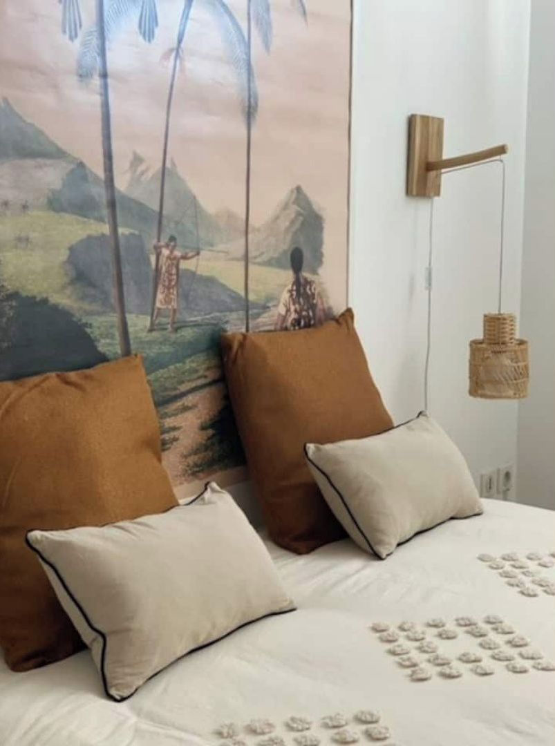 Una cama con dos almohadas, una lámpara colgante y un estante de madera en la pared.