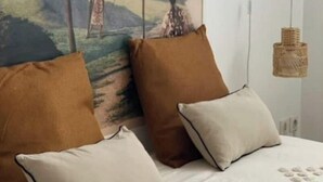 A bed with two pillows, a hanging light fixture, and a wall-mounted wooden shelf. - Appartement Refait Avec Terrasse et vue Montagne (Saint-Denis)
