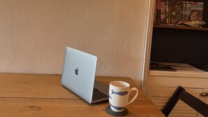 Een houten tafel met een laptop, een notitieboek en een mok. Een wandlamp verlicht de tafel.