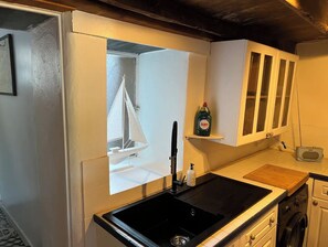 A compact kitchen with a black sink, white cabinets, a small sailboat decoration, and a Fairy dish soap bottle on a shelf.