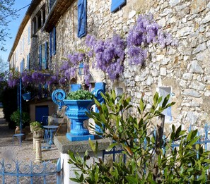 A stone building with blue shutters and purple flowers. There is a blue fountain and a table with chairs in front. - Charming old country house ( 70m2 ) for 2 to 4 persons (Brue-Auriac)