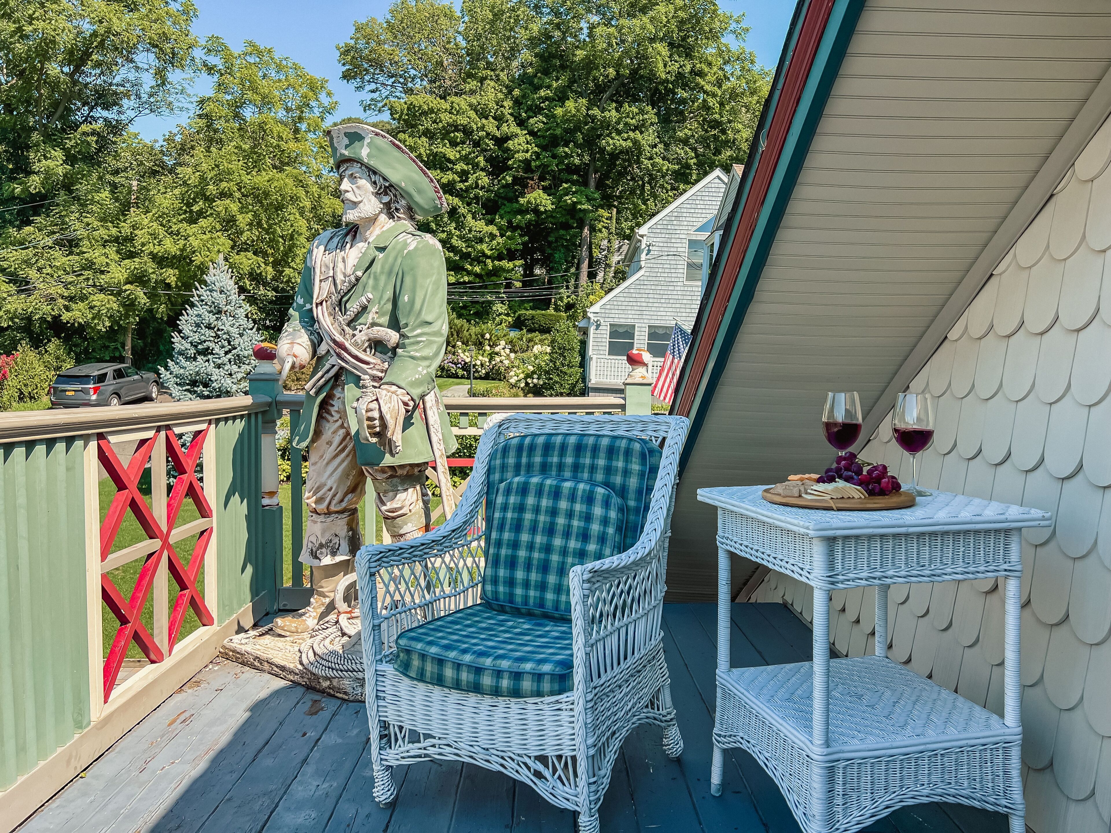 Ein Korbstuhl und ein Tisch auf einer Holzterrasse, im Hintergrund eine Statue.