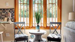 A cozy room with a dining table, two chairs, and a view through large windows. - Captain's Cottage - Cold Spring Harbor Water Views (Cold Spring Harbor)