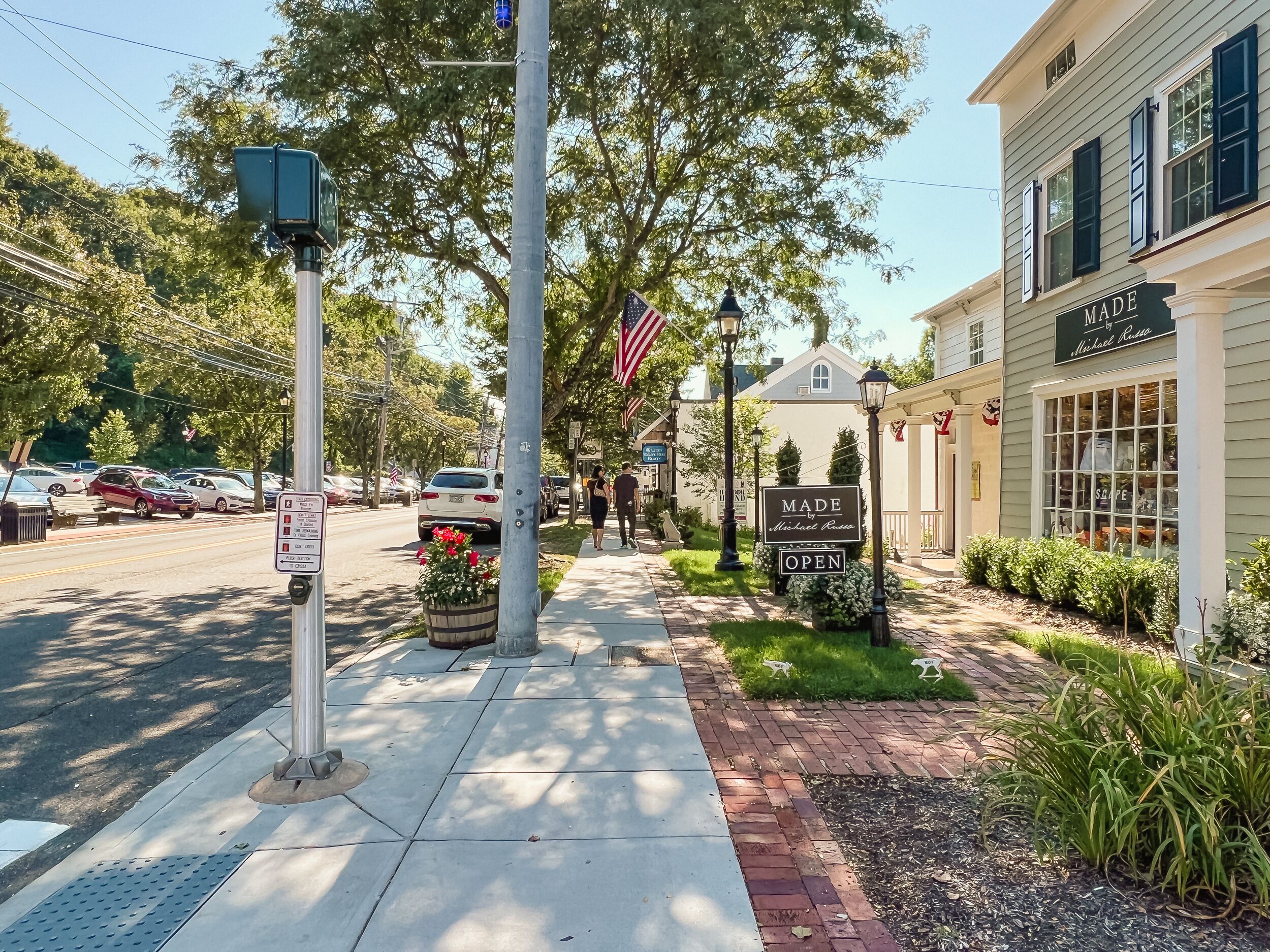 A sidewalk with a sign indicating a business is open, a street with parked cars, and a building with a sign reading "MADE by Michael Rose."