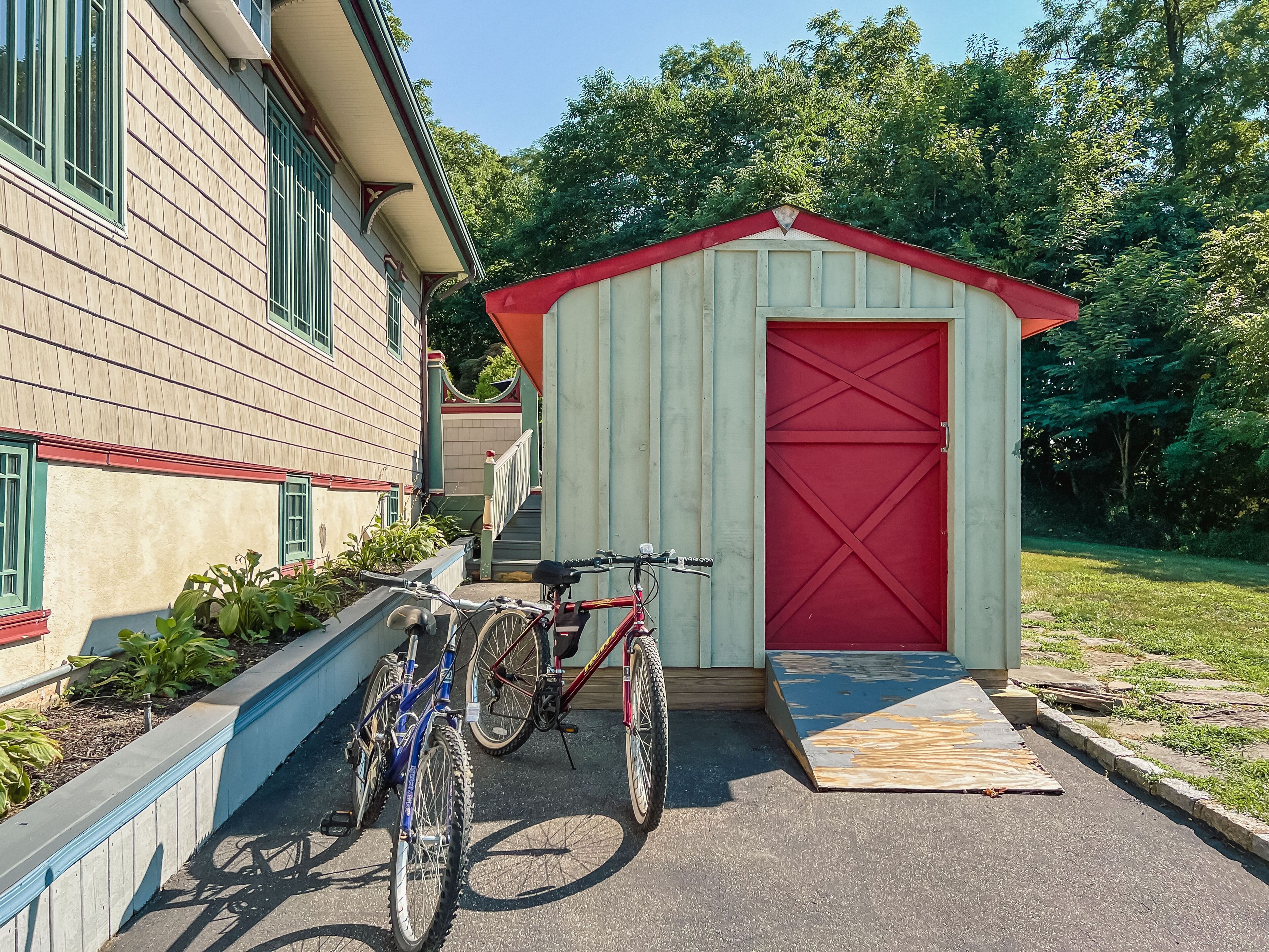 Ein kleines Gartenhaus mit roter Tür, ein Fahrrad davor und eine Holzterrasse.
