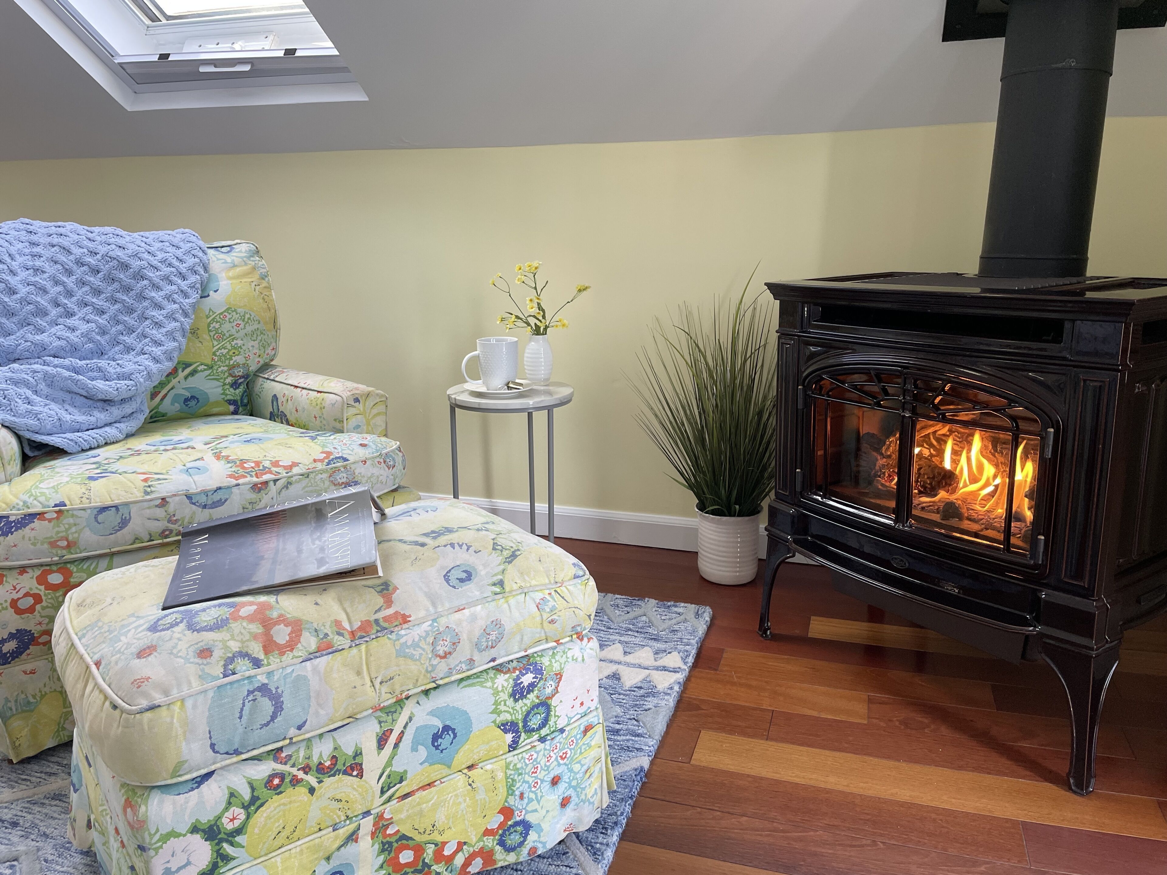 A cozy living room with a fireplace, floral-patterned furniture, and a skylight.
