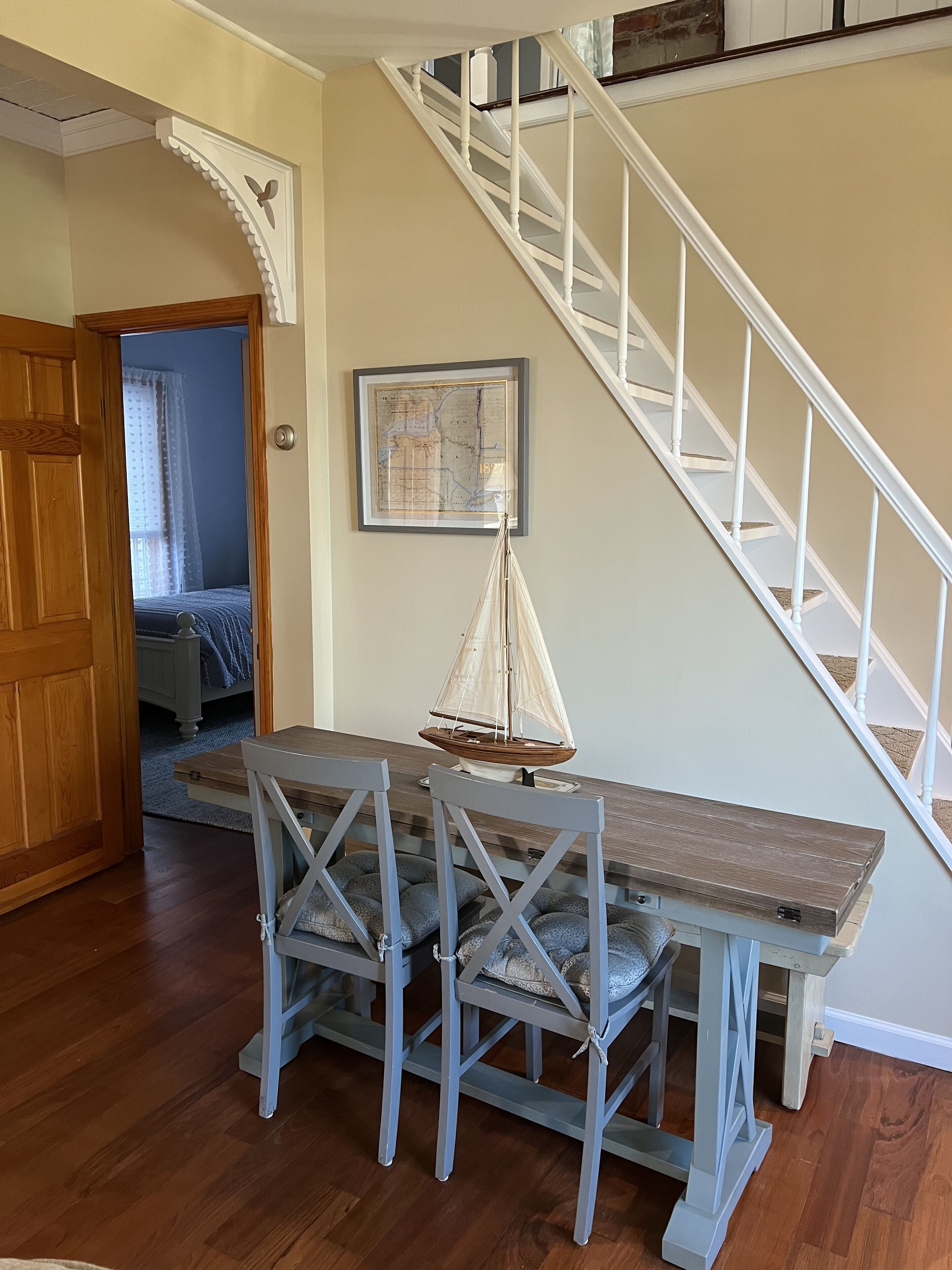 A dining area with a wooden table and chairs, a sailboat model, and a staircase with white railings.