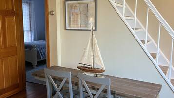 A dining area with a wooden table and chairs, a sailboat model, and a staircase with white railings.