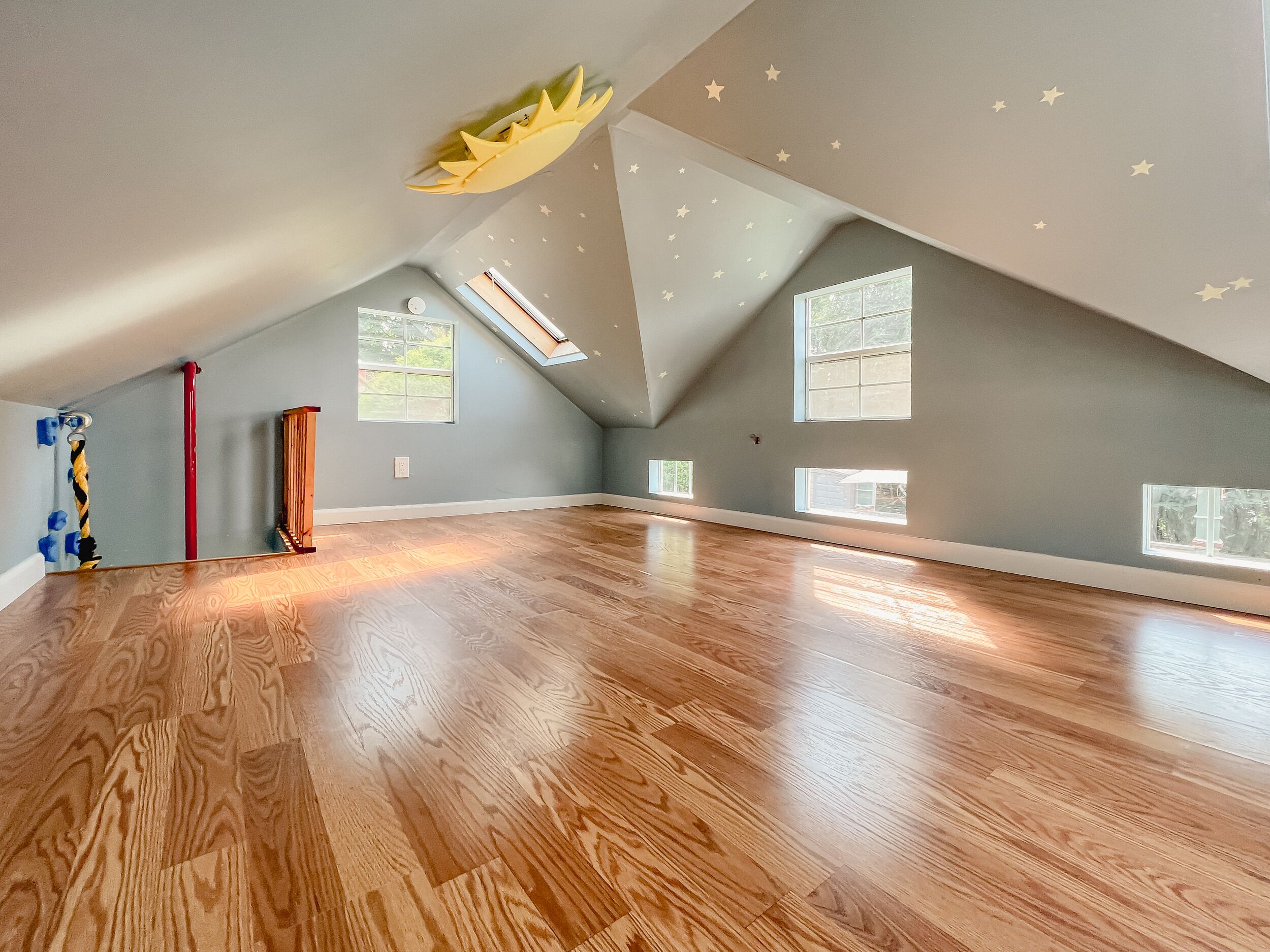 Ein geräumiges Dachzimmer mit schrägen Wänden, großen Fenstern und Holzboden.