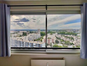 A room with a large window overlooking a cityscape, featuring modern buildings and a distant view of a larger structure.