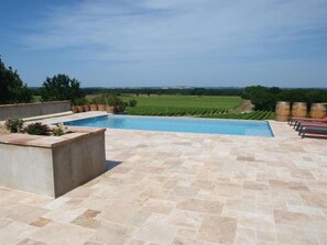 Una piscina al aire libre con solárium de piedra, rodeada por un viñedo, y un cielo despejado.
