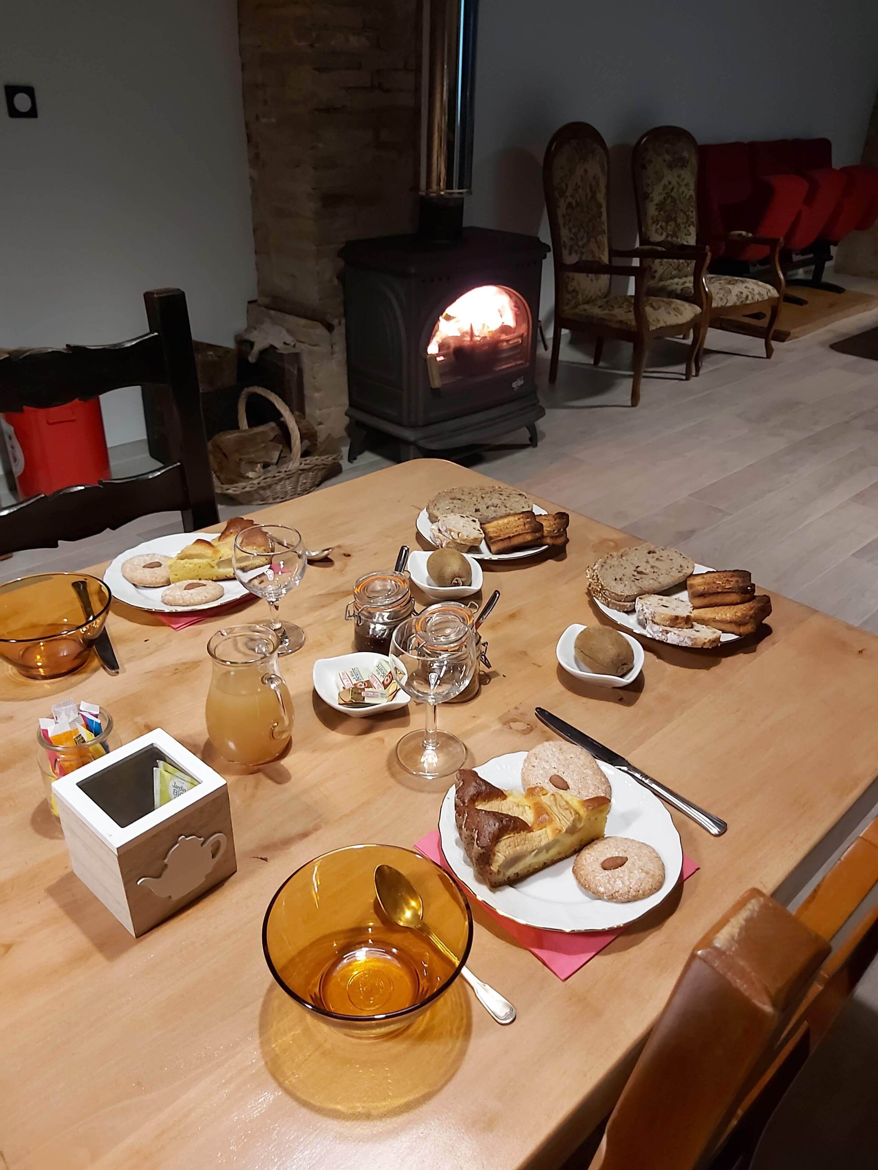Une table à manger dressée avec divers plats et boissons, un poêle à bois en arrière-plan et un coin salon confortable avec des chaises et un canapé.