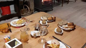 Une table à manger dressée avec divers plats et boissons, un poêle à bois en arrière-plan et un coin salon confortable avec des chaises et un canapé.