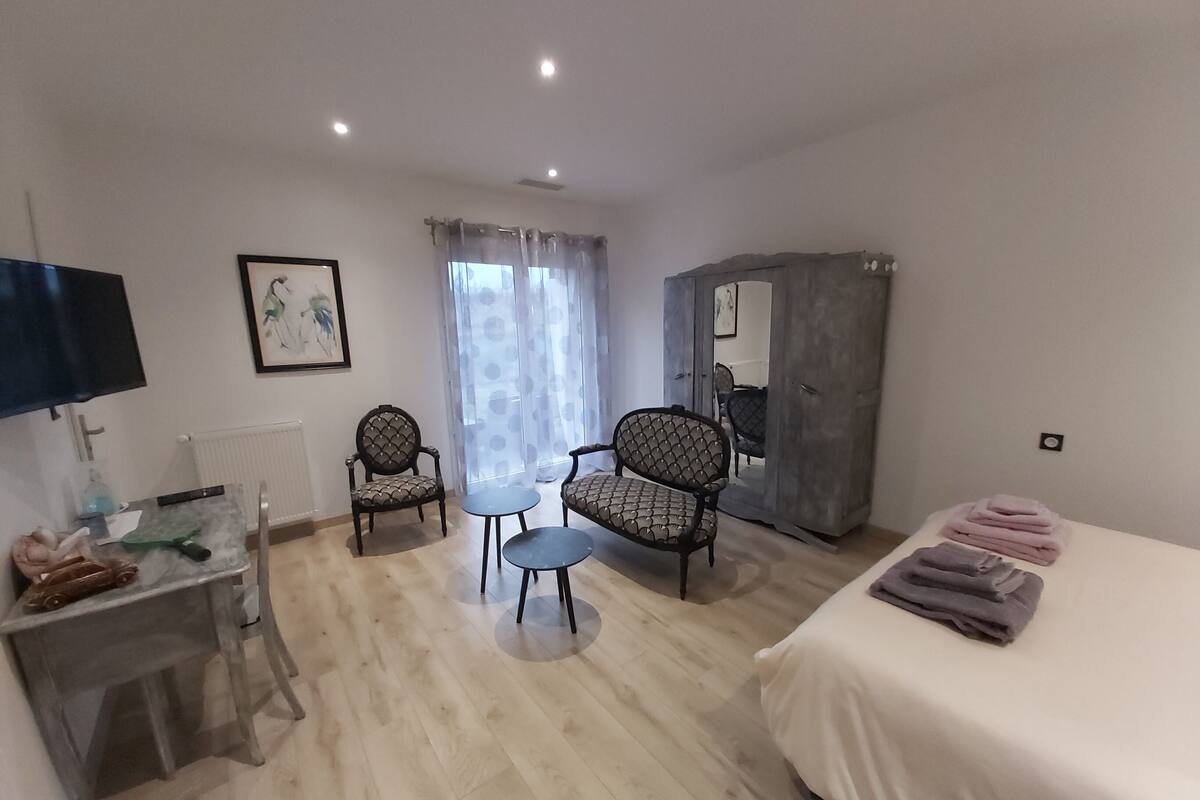 A hotel room with a bed, two chairs, a small table, a TV, a radiator, and a wardrobe.