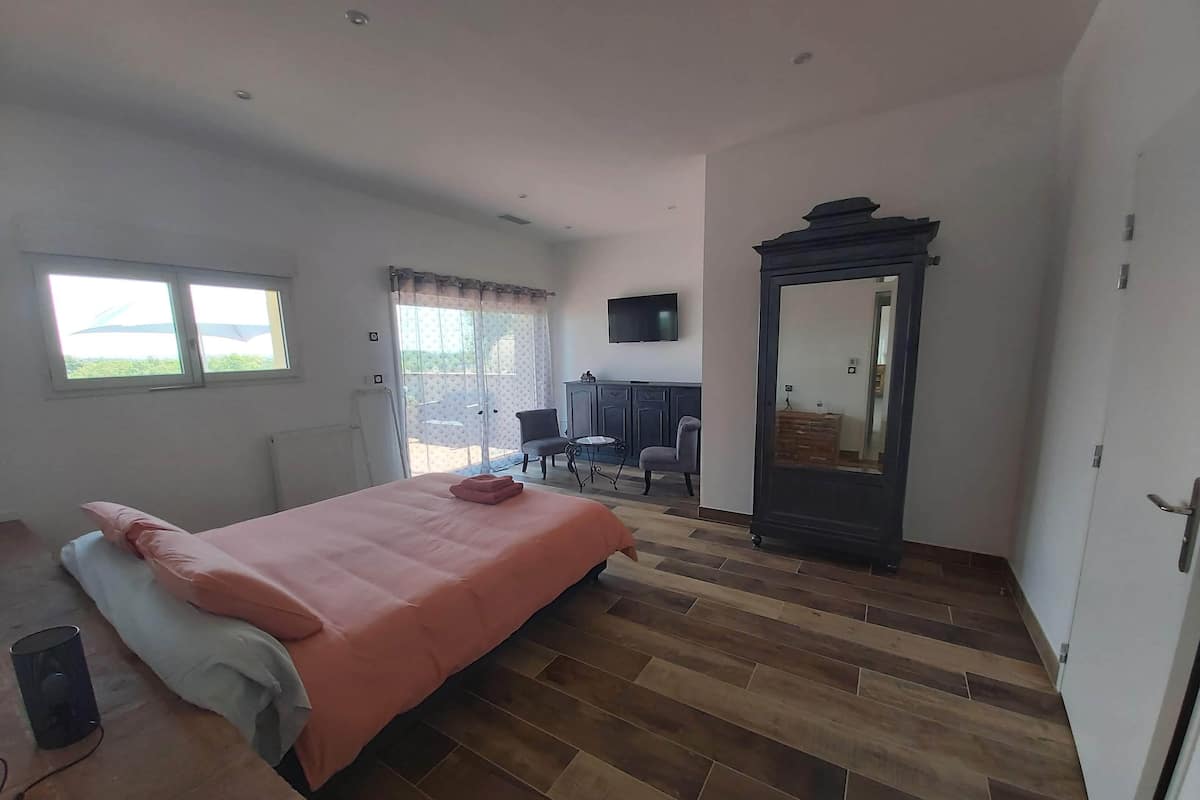 A bedroom with a bed, a desk, a chair, a mirror, and a window.