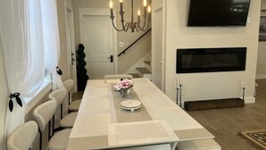 Een eetruimte met een lange tafel, stoelen, een kroonluchter, een flatscreen televisie en een open haard.