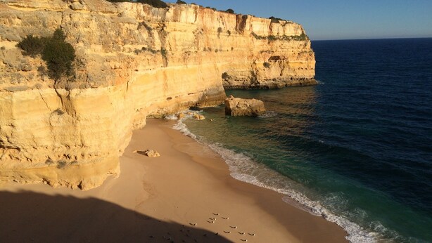 Une plage côtière bordée d’une falaise rocheuse et baignée par une mer d’un bleu limpide.
