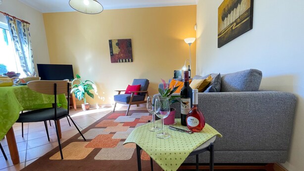 A living room with a grey sofa, a dining table with a green tablecloth, a laptop, and a potted plant. - 2 bedroom independent apartment at Spectacular villa, Pool,Air Con near Old Town (Albufeira)