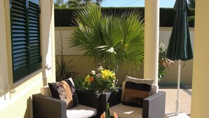 Un espace patio aménagé avec des meubles en osier, une table dressée avec des assiettes et des verres, et un pot de fleurs orné de fleurs jaunes.