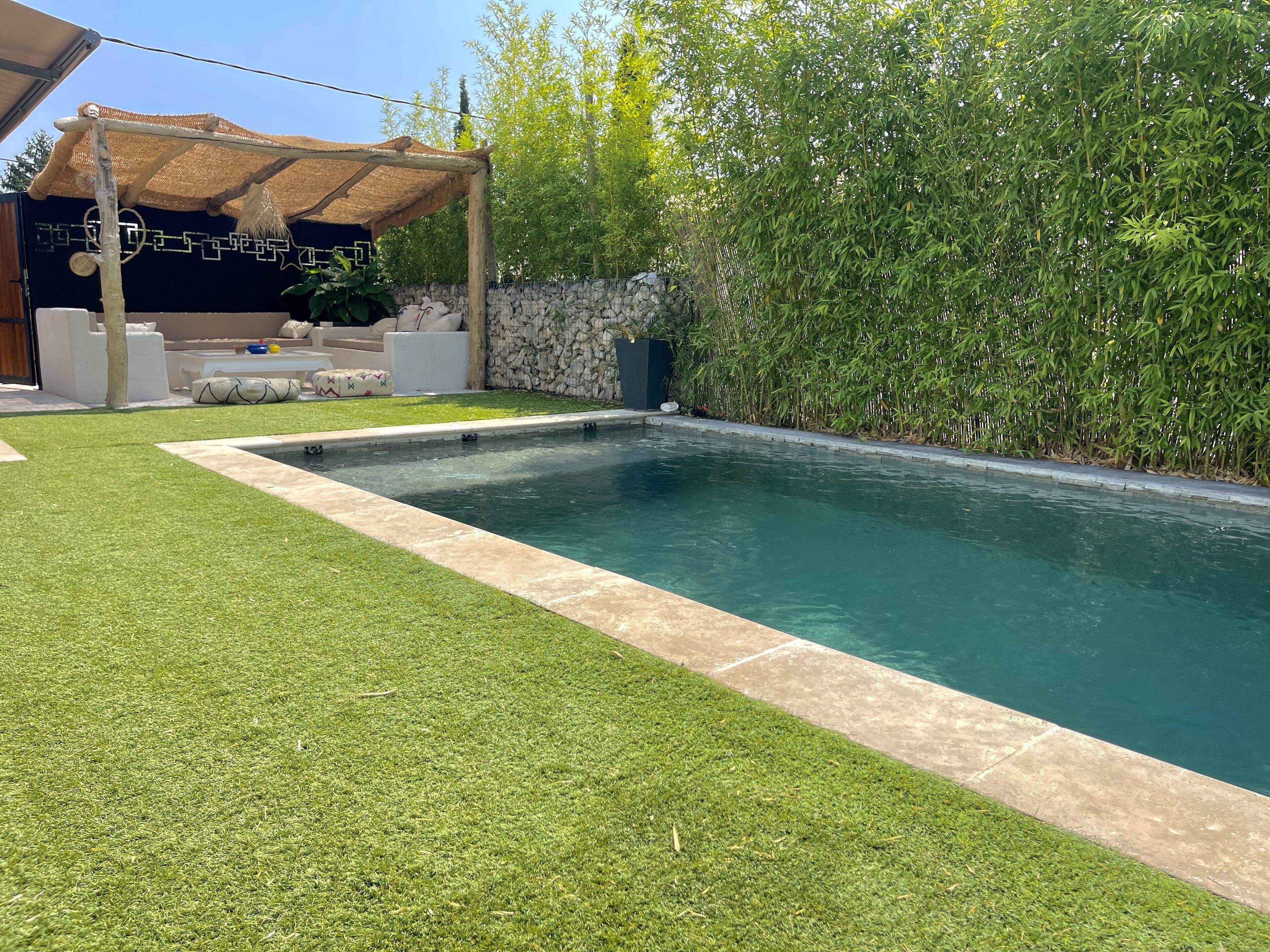 A rectangular swimming pool with a stone border, surrounded by well-maintained grass and bamboo plants.