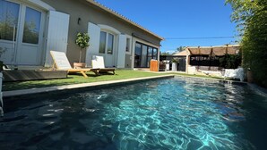 Una piscina con agua cristalina, un porche cubierto y una casa con ventanas amplias y un espacio al aire libre techado.