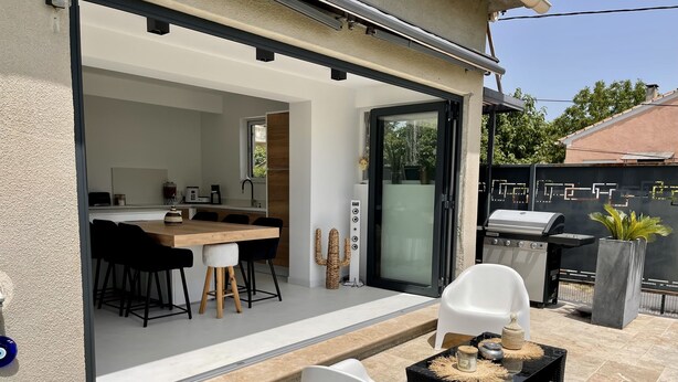 Un patio moderno al aire libre con zona de comedor, una parrilla y una silla blanca.