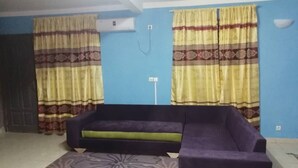 A living room with a purple sofa, yellow curtains with a pattern, and a blue wall.
