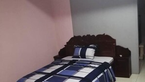 A bedroom with a bed, wooden headboard, and a pink wall.