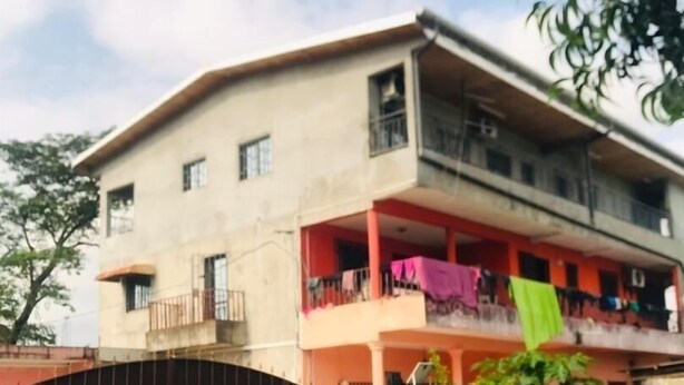 A two-story building with a flat roof and a balcony on the ground floor.