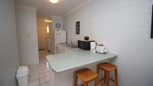 Uma cozinha compacta com armários brancos, micro-ondas, torradeira e dois banquinhos de madeira.