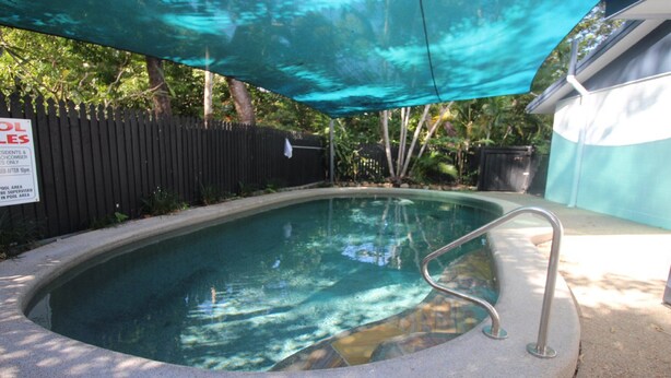 Piscina com escada de metal, cercada por uma vedação e árvores.