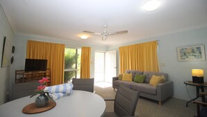 Sala de estar com sofá, televisão, mesa de jantar com um vaso de flores e ventilador de teto.